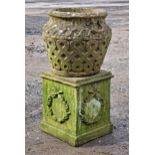 A weathered reconstituted stone garden planter with repeating lattice detail raised on a square