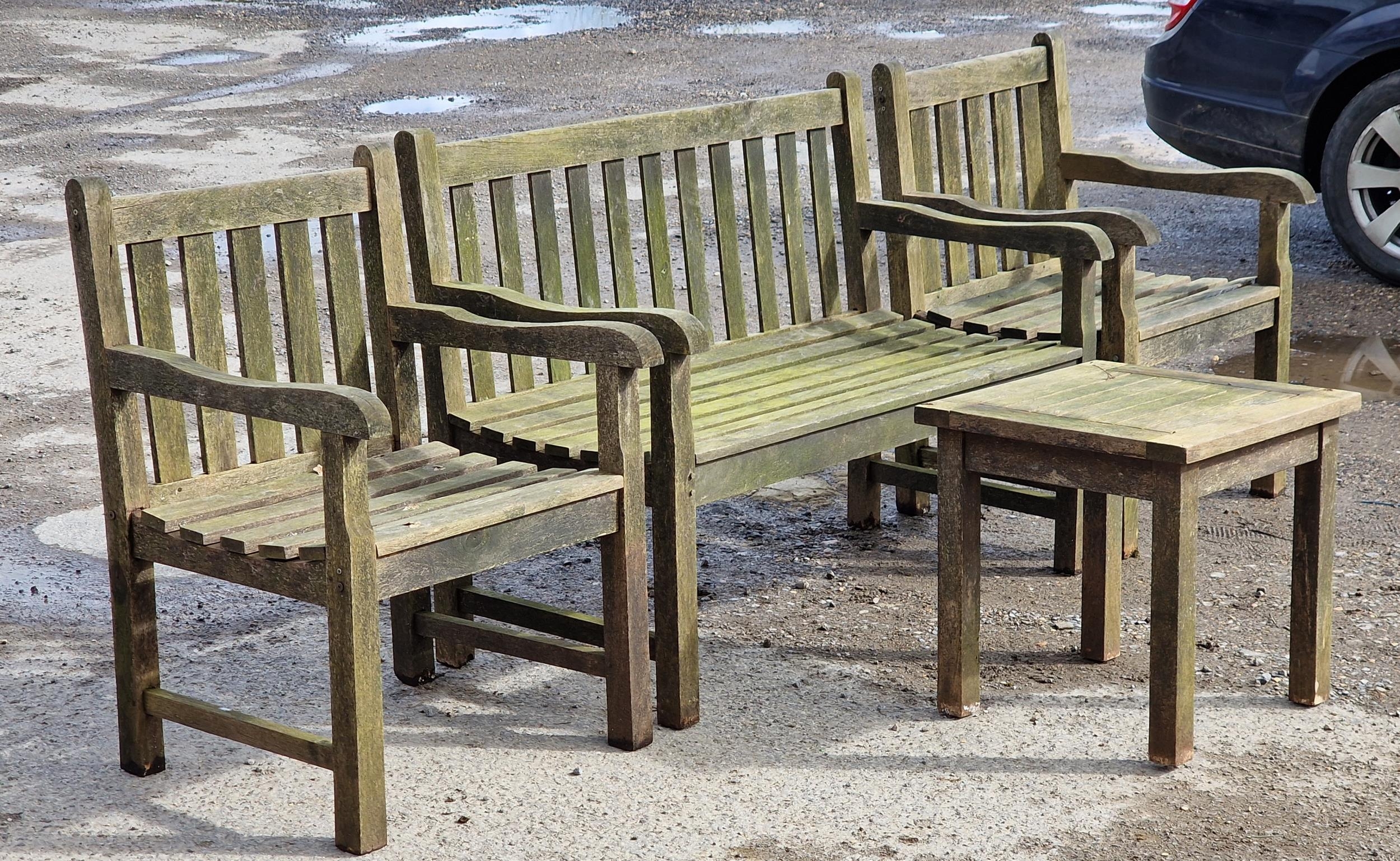 A weathered teak garden suite with slatted seats and backs to include two armchairs, a bench and a