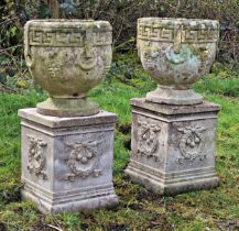 A pair of weathered reconstituted stone garden urns with Greek Key and grape detail raised on