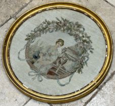 19th century woolwork portrait of a seated lady in a garden setting within a wreath, 48cm