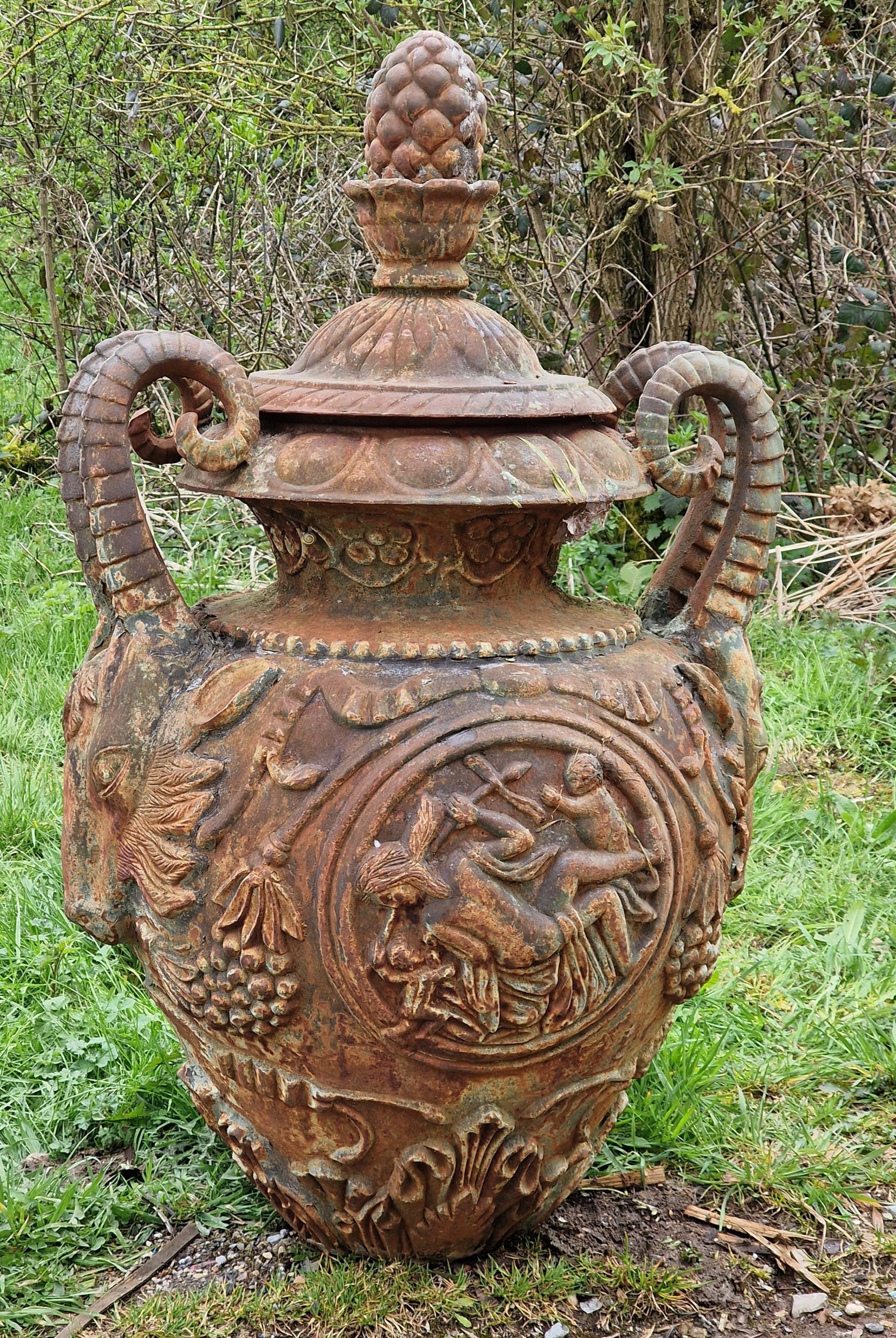 A good quality ornate cast iron garden urn with rams head handles, pineapple finial and foliate