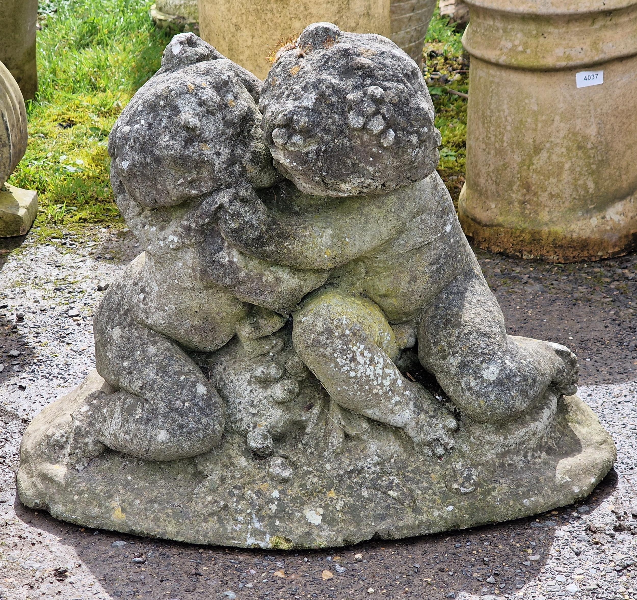 A weathered reconstituted stone garden ornament of cherubs embracing, H 45cm x W 66cm