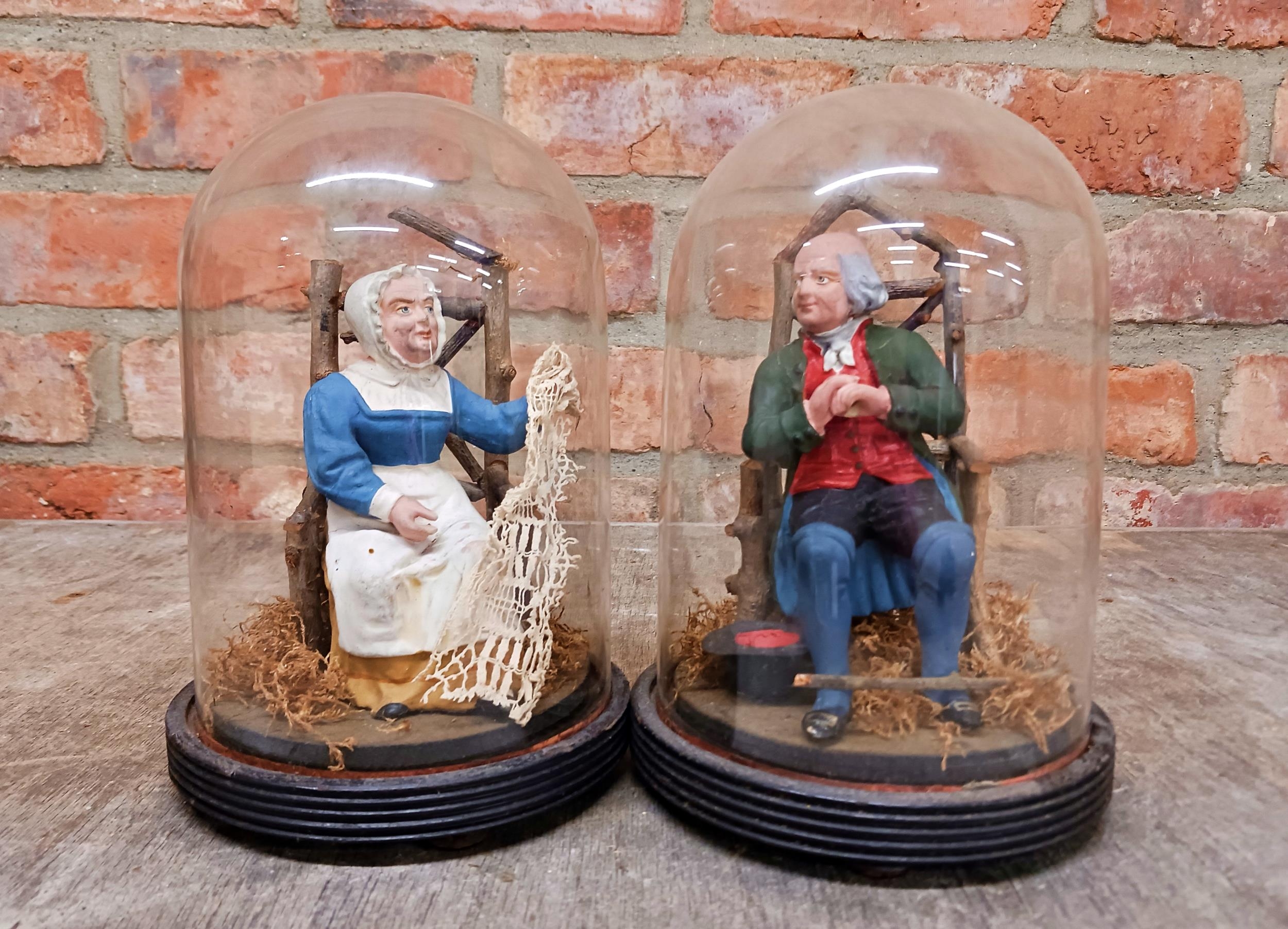 Pair of hand painted pottery figures of seated husband and seamstress wife held in original glass
