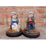 Pair of hand painted pottery figures of seated husband and seamstress wife held in original glass