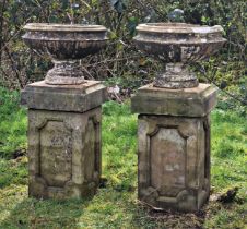 A Pair of reconstituted stone garden urns raised on associated square cut pedestals with fielded