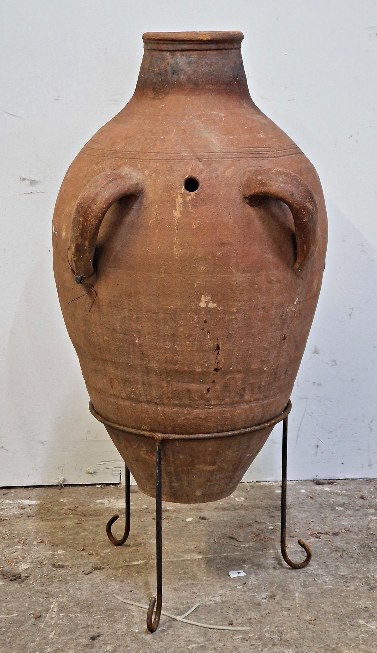 A terracotta amphora with twin loop handles and incised detail, raised on a wrought iron stand, H