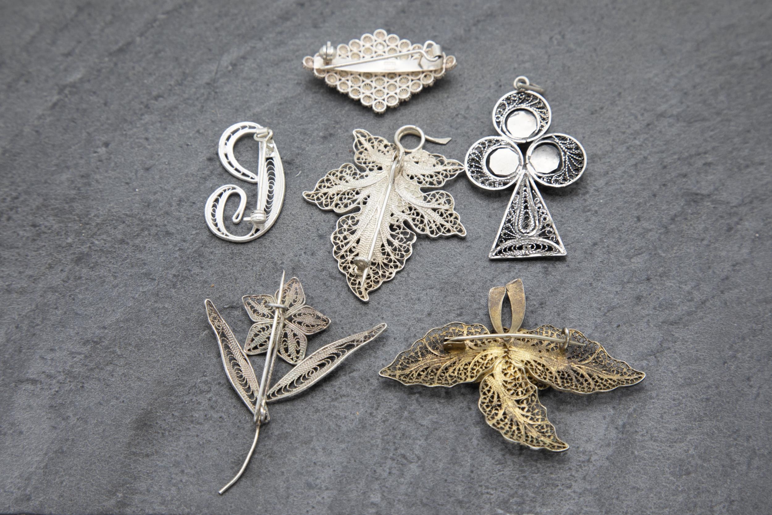 Six filigree silver brooches or pendants to include turquoise inset club pendant and enamelled