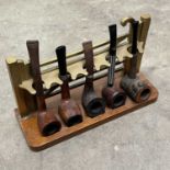 A vintage brass pipe rack in the form of a field gate, oak plinth, 24cm wide, with five pipes