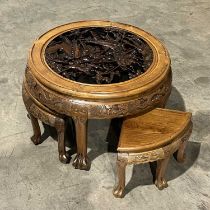 A Chinese circular carved low table, with four integral stools and a glass top above a carved battle