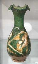 A Chinese earthenware vase, probably Tang, carved with flowers and petals and glazed in green,