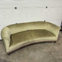 An Edwardian curved sofa, sage green upholstery, splayed arms, and raised on ogee block supports and