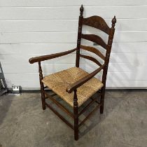 A ladder back armchair, with a rush seat, carved top rail, and two finials, together with a matching