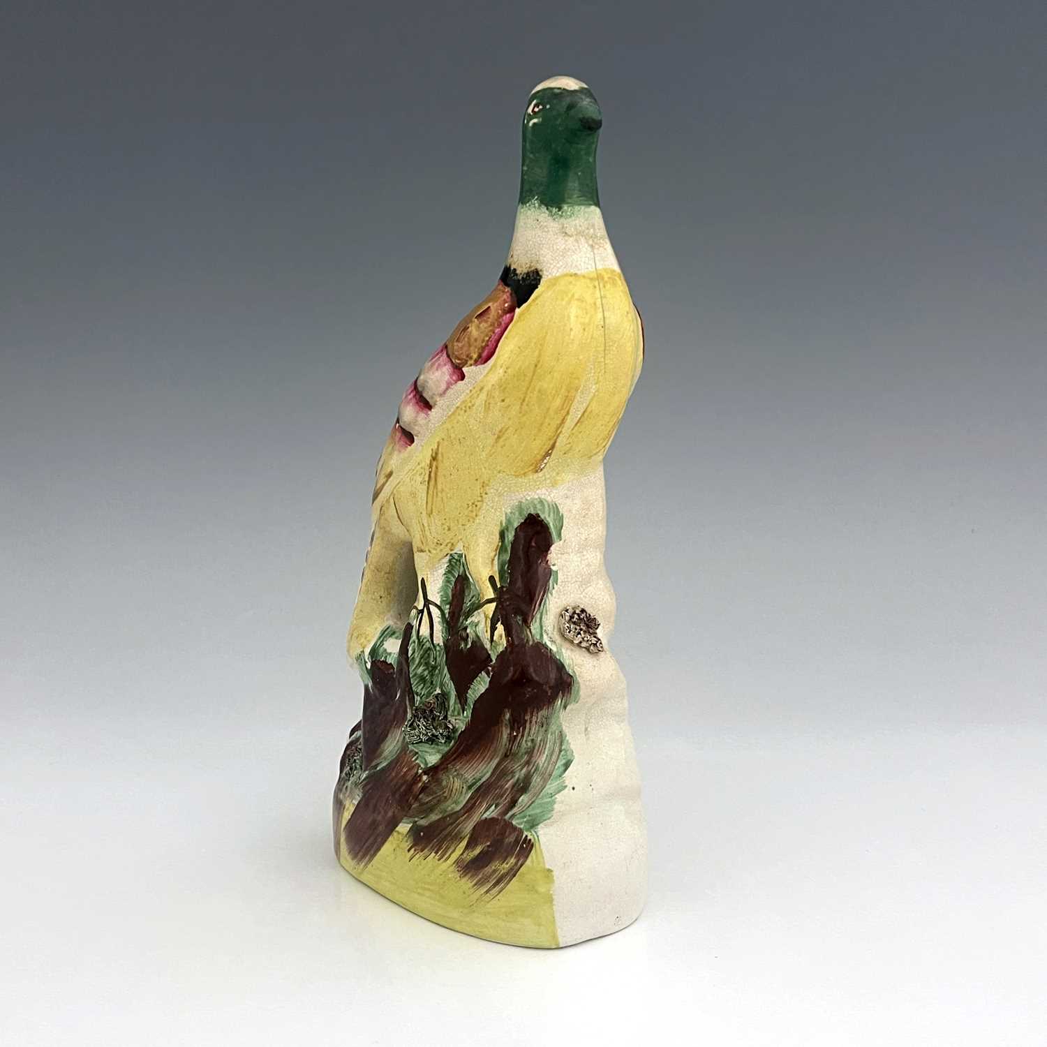 A Staffordshire pottery exotic bird, circa 1850, modelled perched on a green and brown mound, on