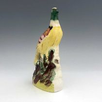 A Staffordshire pottery exotic bird, circa 1850, modelled perched on a green and brown mound, on