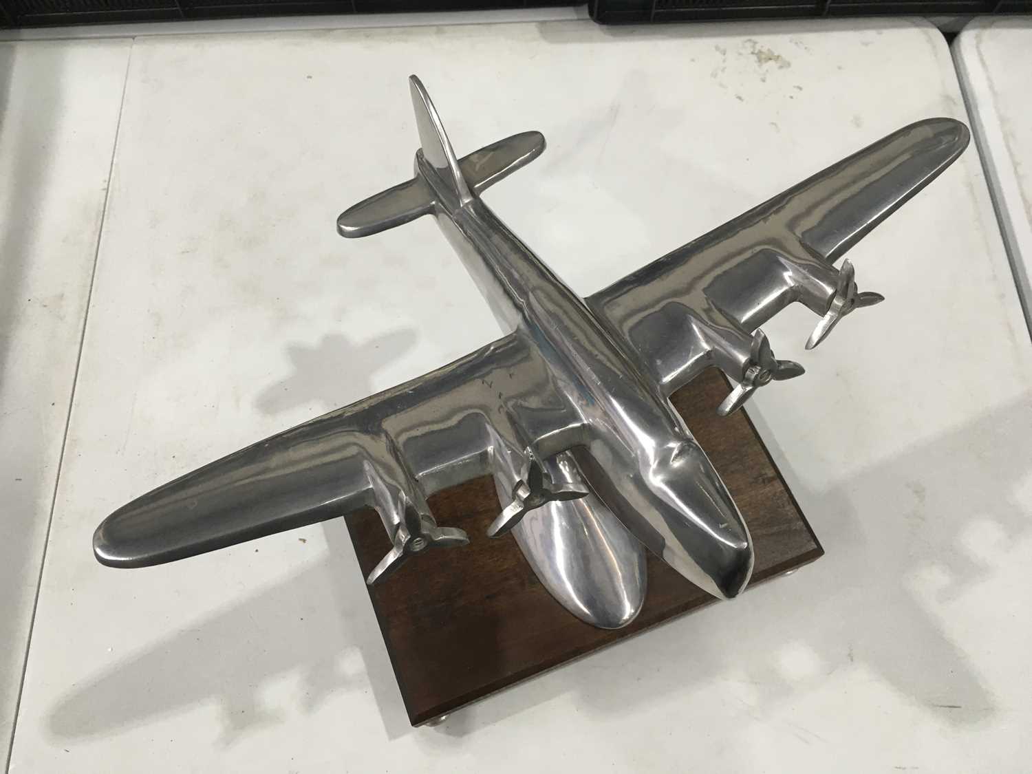 A cast metal model of a flying boat seaplane, on bracket stem and oval base, mounted on wooden stand