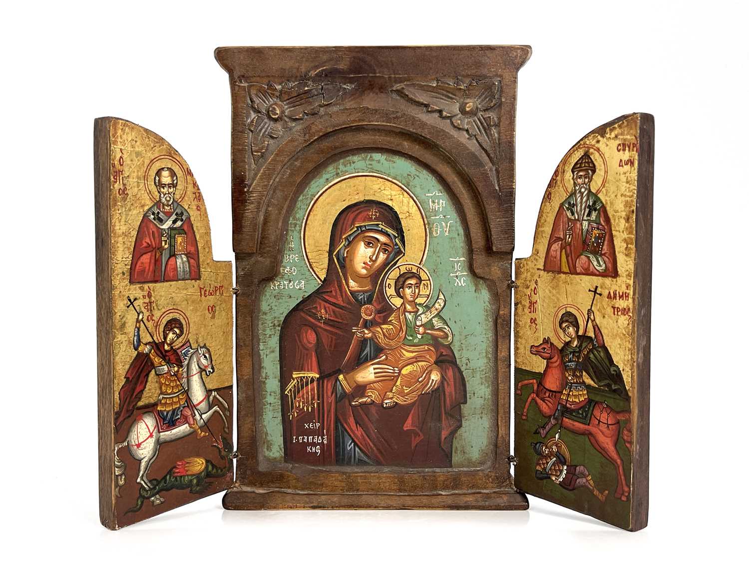 A Greek Orthodox triptych ikon, wooden frame with leaf-carved spandrels to the pediment, hinged