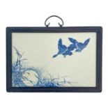 A Japanese blue and white painted plaque, decorated with ducks flying over a wetland scene, framed