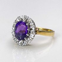 An 18 carat gold and amethyst cluster ring, the central purple stone within a band of diamonds,