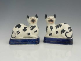 A pair of Staffordshire pottery cats, mid 19th century, modelled seated, on blue bases, black sponge