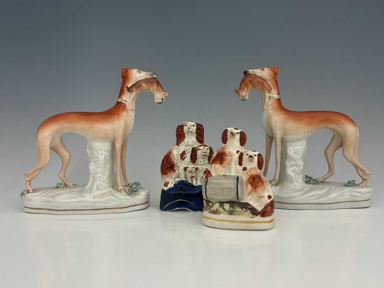 A pair of Staffordshire pottery figures of greyhounds, modelled standing, holding rabbits, on tufted