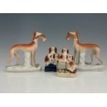 A pair of Staffordshire pottery figures of greyhounds, modelled standing, holding rabbits, on tufted