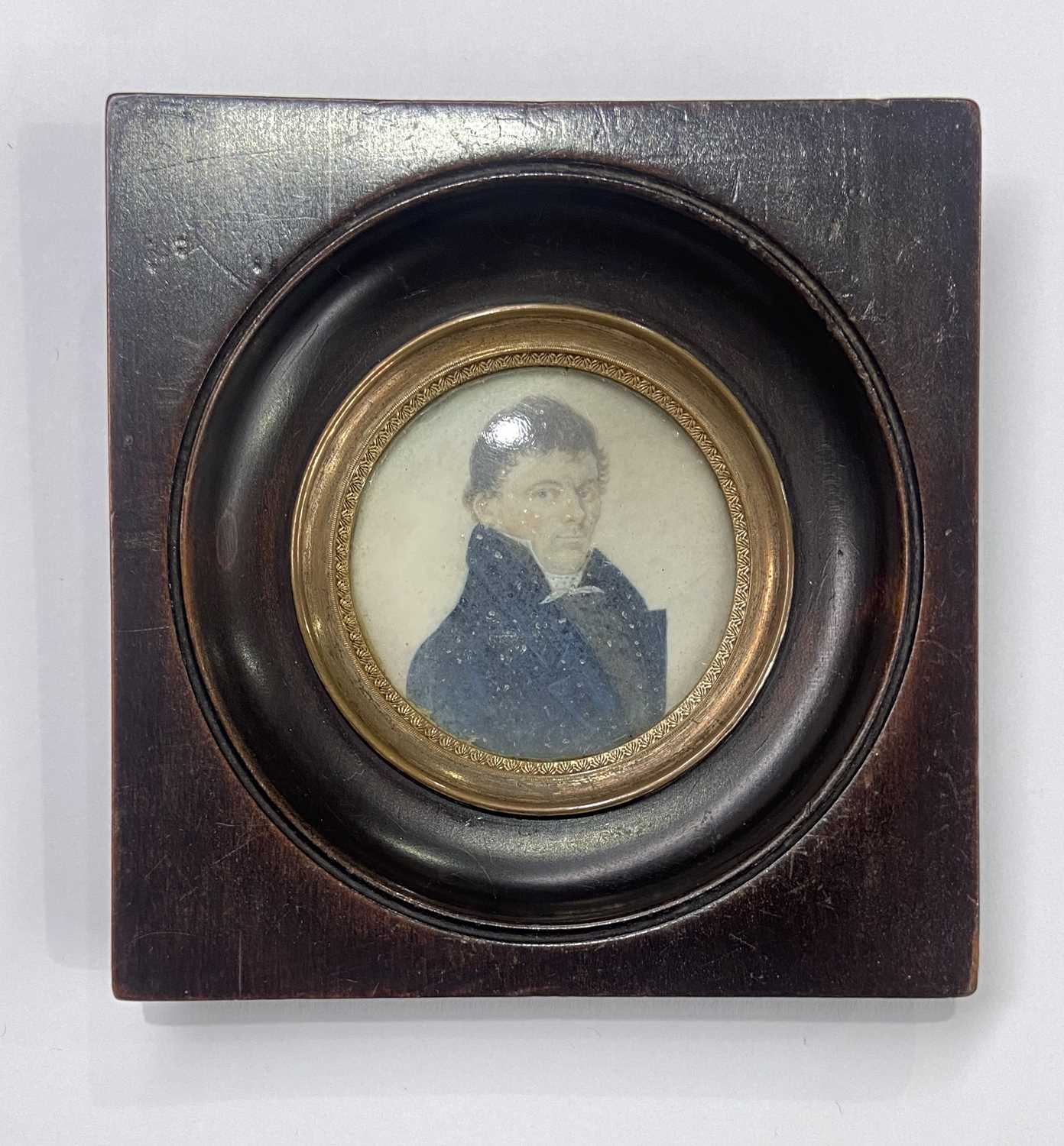 An early 19th century portrait miniature painted to depict a man in a high-collared blue coat, on