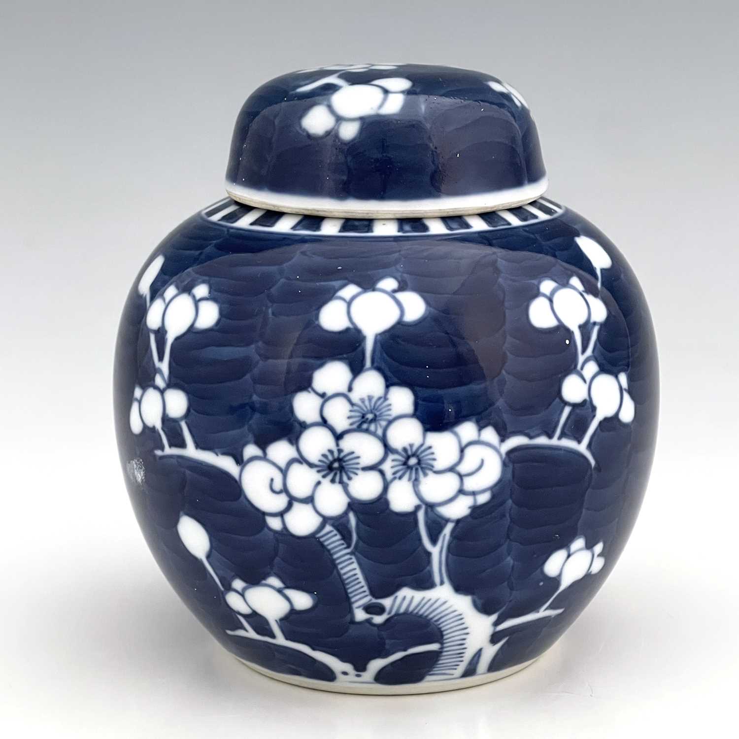A Chinese blue and white ginger jar and cover, painted with prunus blossom on a blue wavy ground,