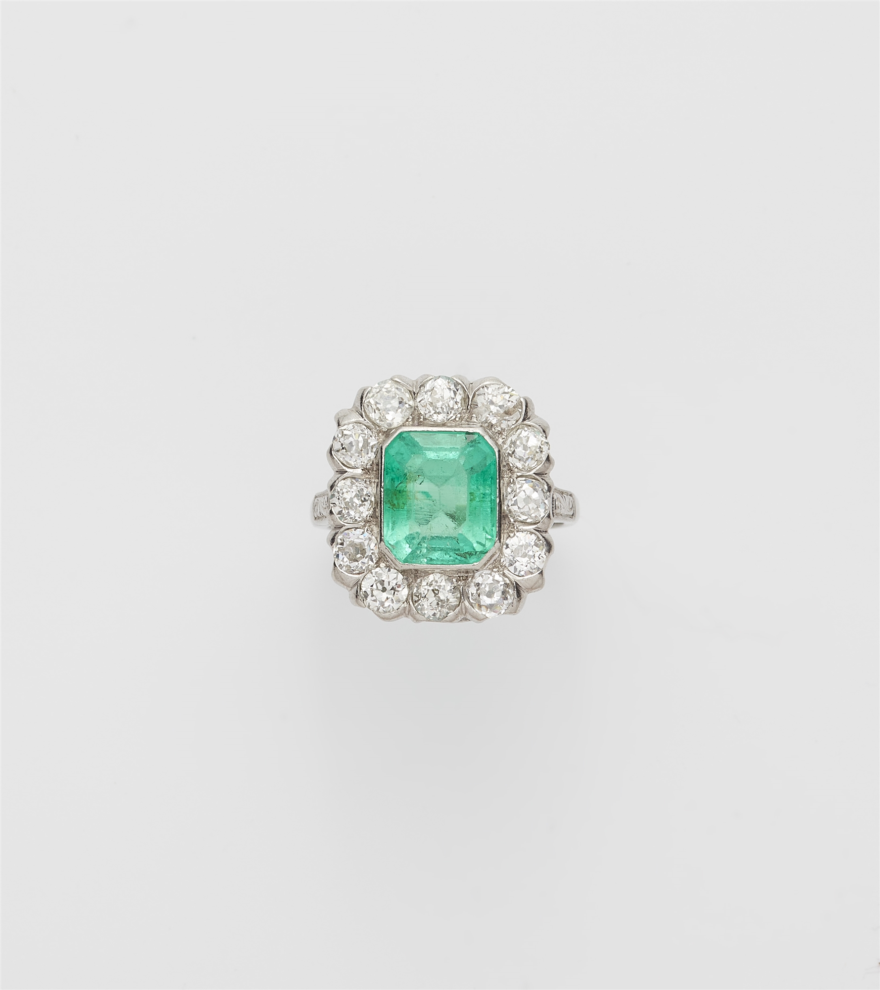An Art Déco platinum iridium diamond and emerald cluster ring.