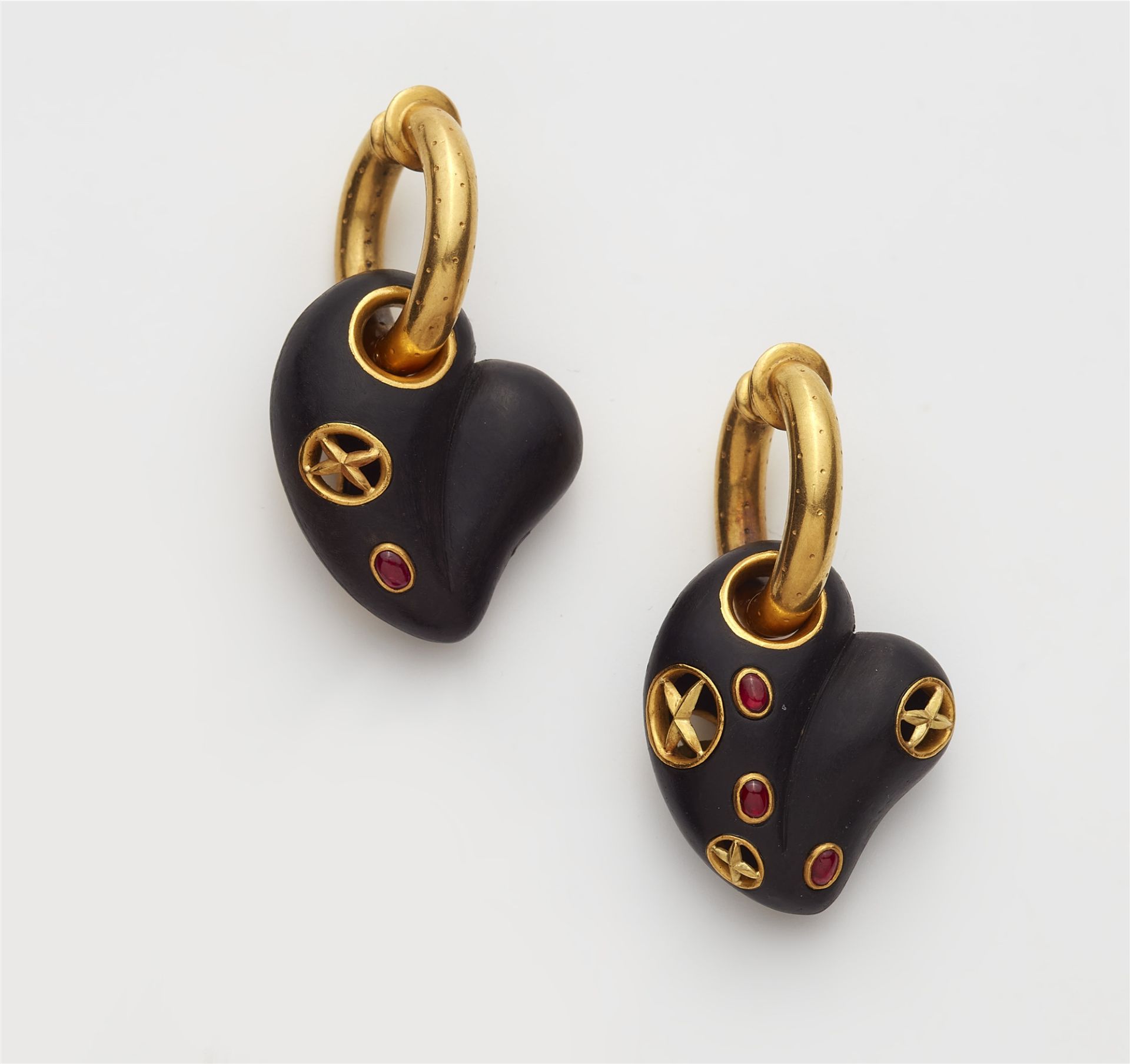 A pair of 18kt gold hoop earrings with ruby set carved ebony heart pendants.