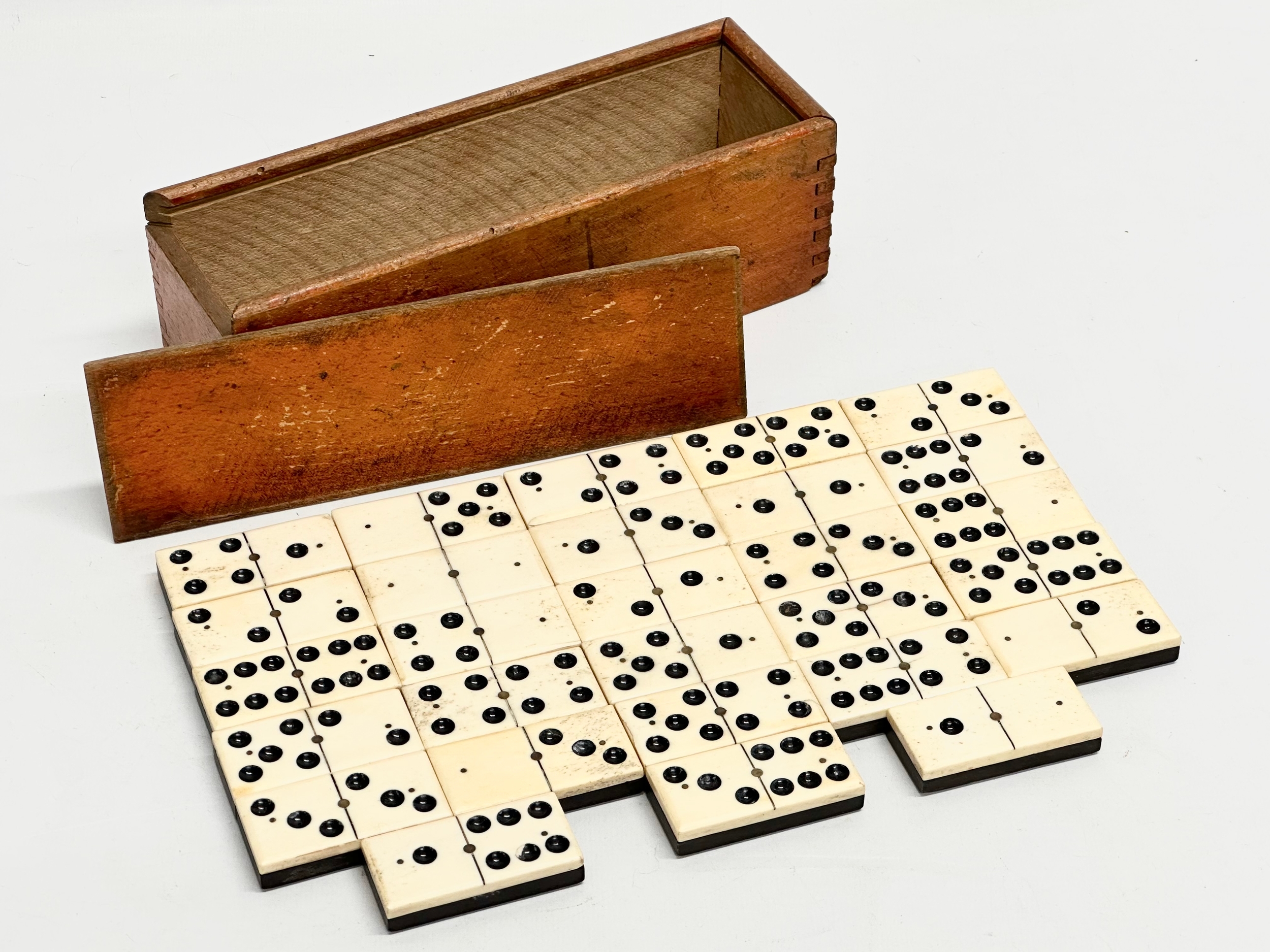 A collection of 19th Century bone and ebony dominoes with wooden box. Pieces 5.5cm. Box 21cm.