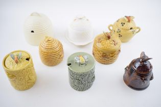 A collection of pottery honey pots in varying forms and colours to include a Wedgwood Queensware