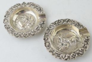 A pair of sterling silver ashtrays with embossed scenes to include cows resting and a man dressed in