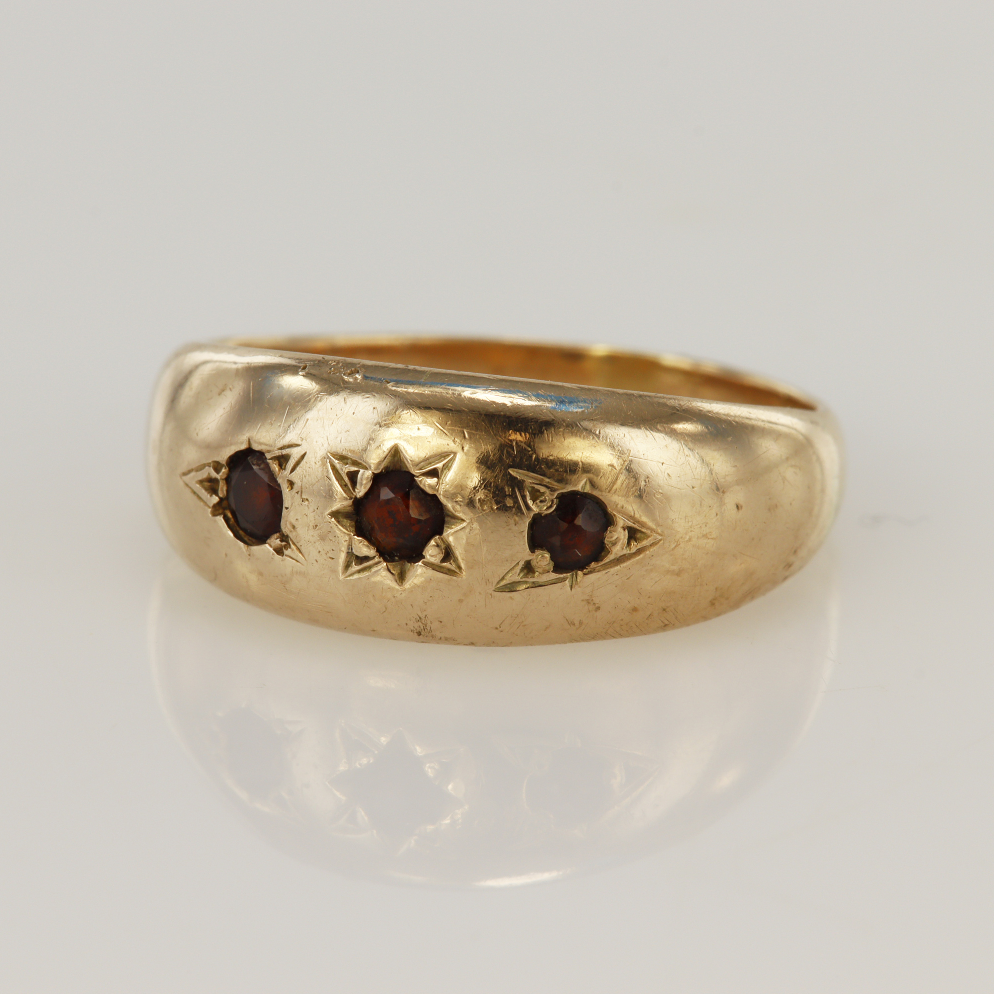 Yellow gold (tests 9ct) garnet gypsy ring, three star set garnets, principle measures 3mm, head