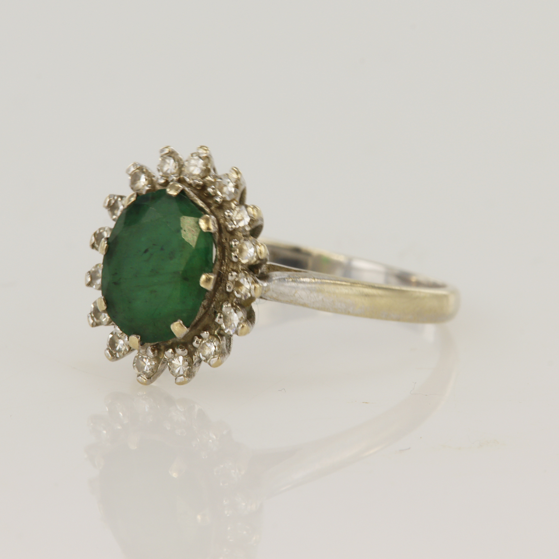 White gold (tests 18ct) diamond and emerald cluster ring, one oval emerald measuring 8x7mm,