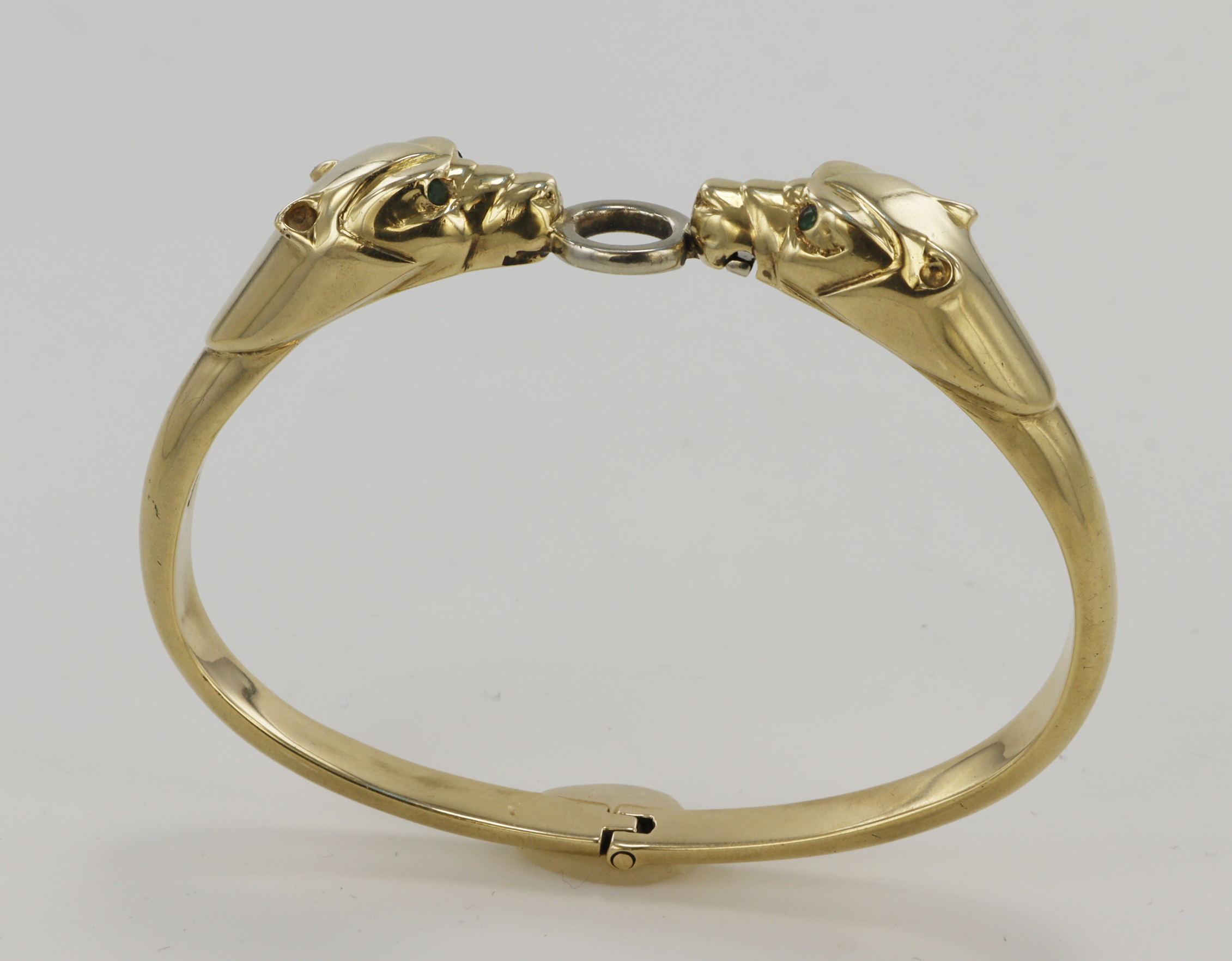 Stamped 14ct yellow gold hinged bangle depicting two panther heads with emerald eyes holding a white