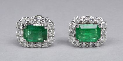 A pair of 18ct white gold cluster earrings set emeralds and diamonds - the central step cut emeralds