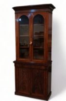 An early Victorian mahogany cabinet bookcase - the raised back with cornice above a pair of arched