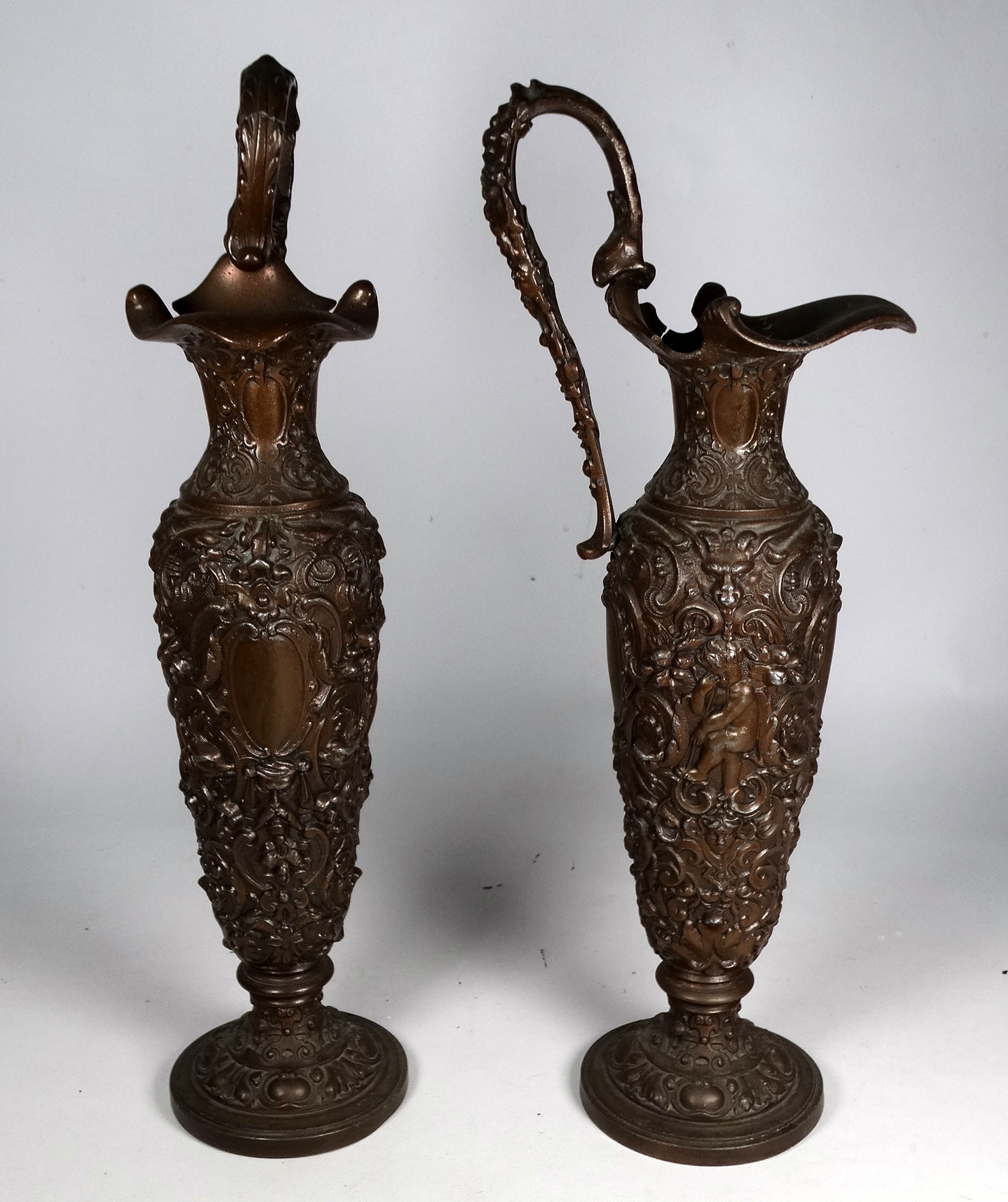 A pair of cast spelter bronzed ewers - in the classical style with masks, cherubs and strapwork,