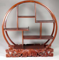 A 20th century hardwood table shelf - circular with asymetrical shelves on a foliate carved stand,