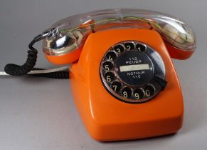 A vintage German telephone - orange body with an illuminated clear receiver handle.