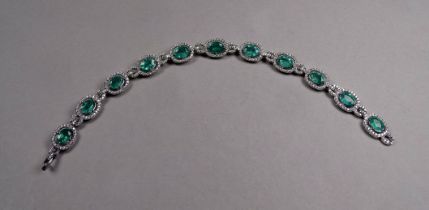 An 18ct white gold emerald and diamond set line bracelet - the oval emeralds weighing 7.12ct