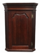 A George III oak corner cupboard - with a dentil moulded cornice above a shaped fielded panel door