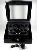 An automatic watch winder - gloss ebonised finish with a curved glass cover enclosing a pair of