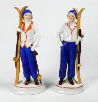 A pair of early 20th century figures - dressed a skiers, standing holding skis, raised on oval