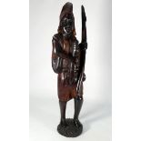 A 20th century African carved hardwood figure, standing holding a spear, with a rifle on his back,