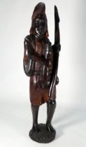 A 20th century African carved hardwood figure, standing holding a spear, with a rifle on his back,