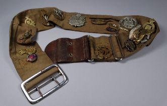 A khaki canvas military belt - set with fourteen various regimental badges and insignia.