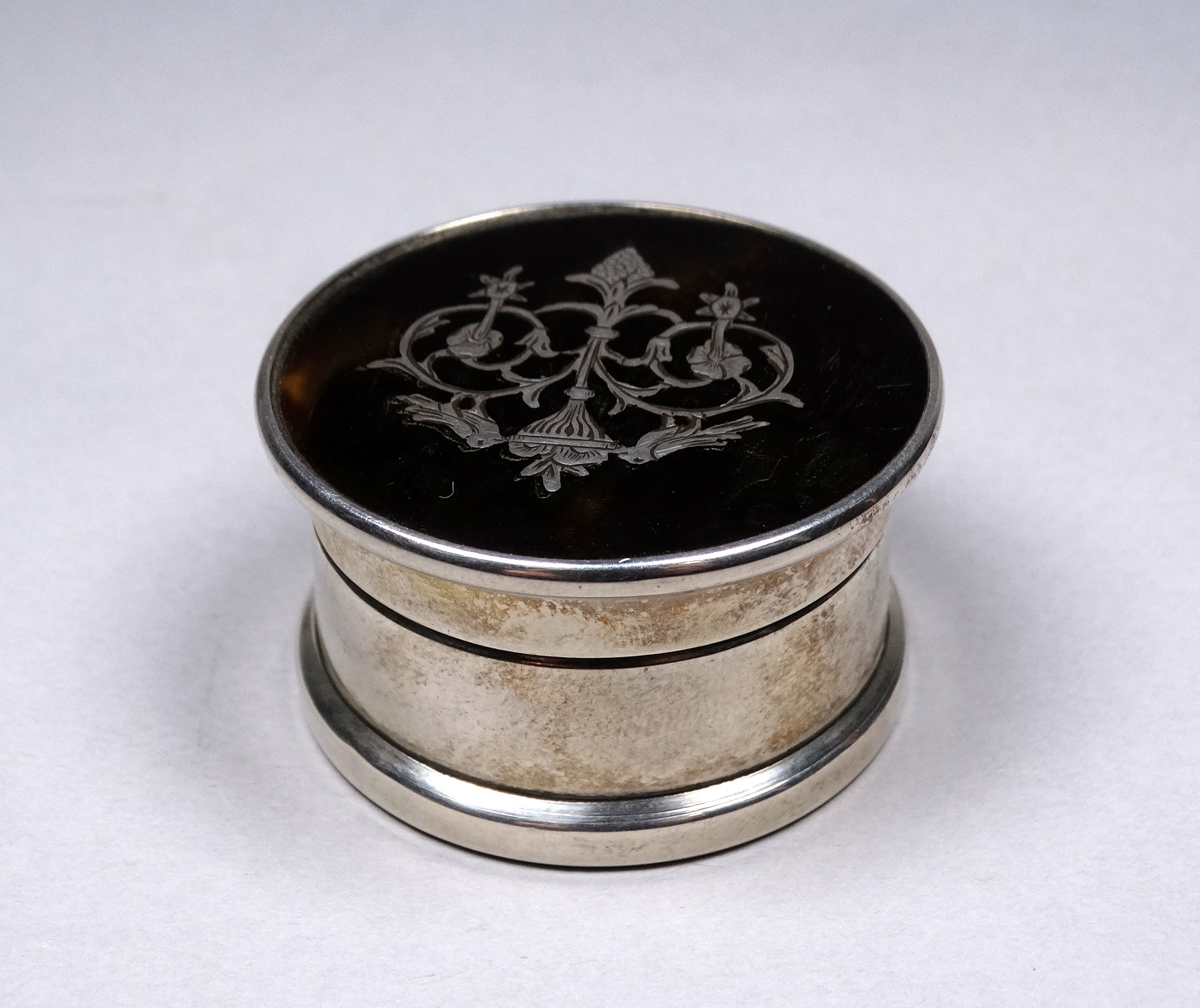 A silver pill box - Birmingham 1917, circular with a tortoiseshell top inset with birds and foliage,
