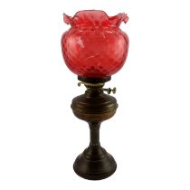 A brass oil lamp with dimpled cranberry glass shade - height 49cm.