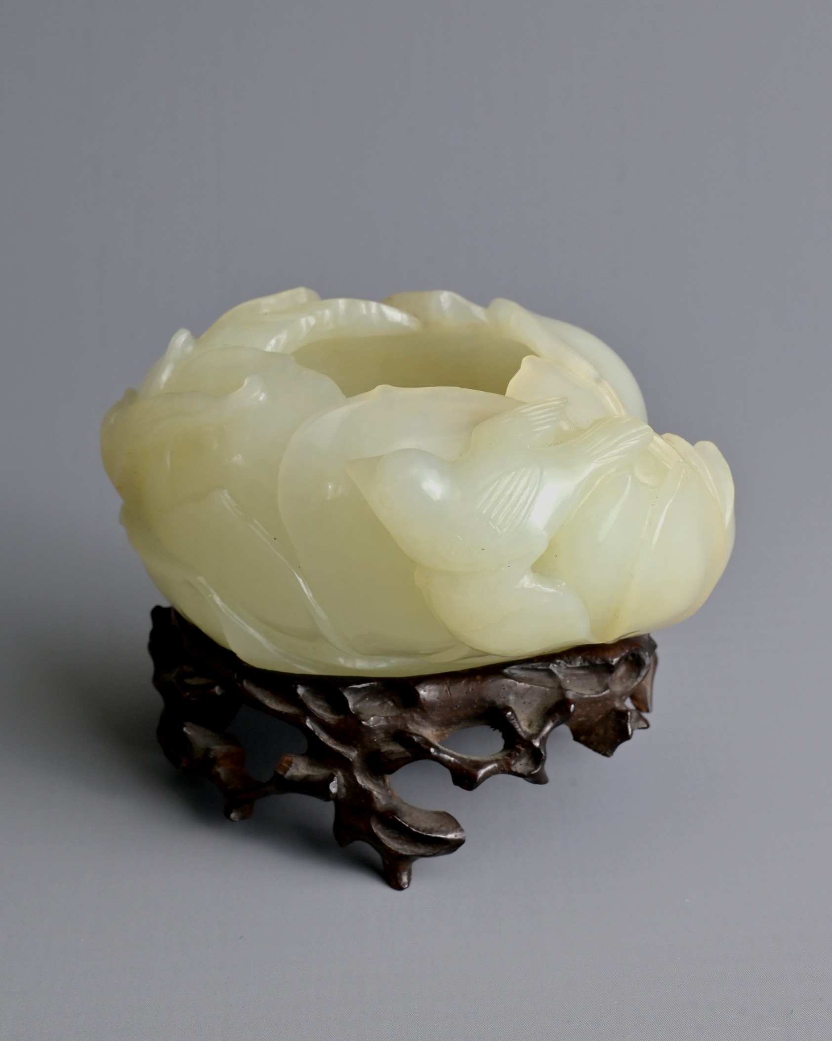 A CHINESE PALE CELADON JADE BRUSH WASHER ON WOODEN STAND, QING DYNASTY. Carved in the form of a